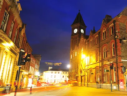 Red brick clock tower and Victorian buildings lit up on a street at dusk in West Berkshire