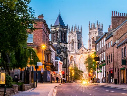 York Minster towers glowing at dusk at the end of a lamplit street in York