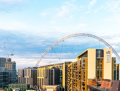 Wembley Stadium arch rising behind modern apartment blocks at sunset in Brent