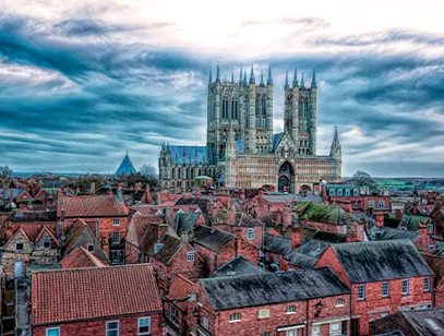 Lincoln Cathedral towering over red-tiled rooftops under a dramatic cloudy sky in Lincolnshire