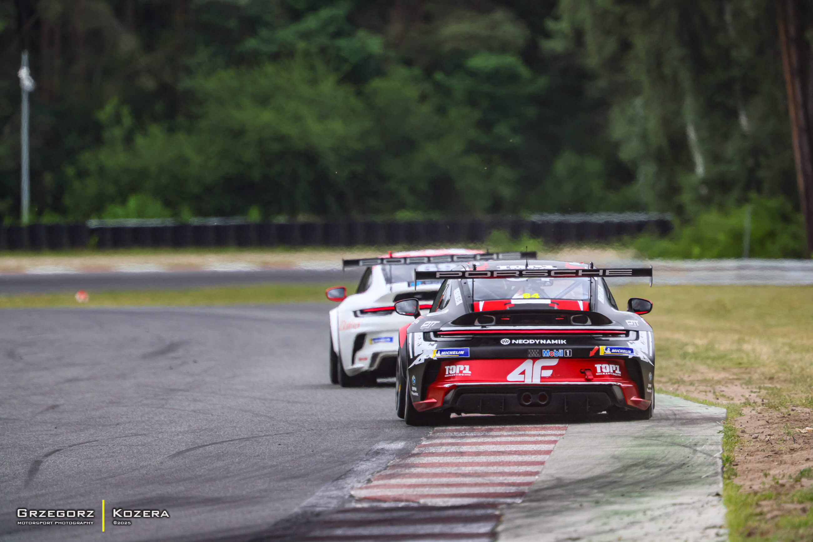 Porsche 911 GT3 Cup Fabiana Dybionki (#44) prowadzi stawkę podczas wyścigu na Torze Poznań, ujęcie od tyłu na zakręcie, z dynamiczną linią wyścigową i otoczeniem leśnym w tle.