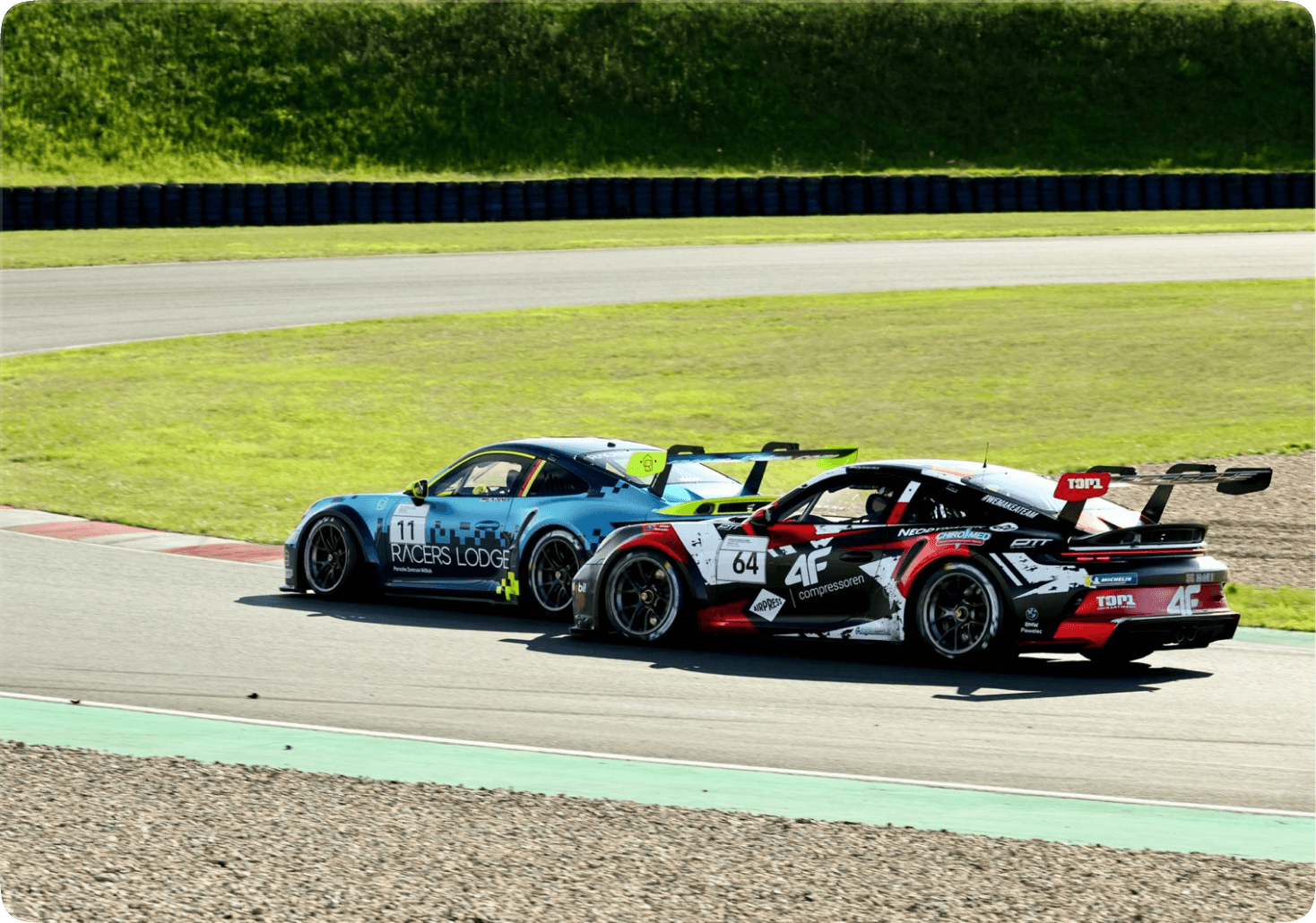 Fabian Dybionka w samochodzie Porsche 911 GT3 Cup z numerem 64 i grafiką rekina toczy zaciętą walkę o pozycję z niebieskim autem konkurenta oznaczonym numerem 11 na torze wyścigowym. Oba pojazdy są w fazie dynamicznego pokonywania zakrętu, a w tle widać zielone wały ochronne toru.