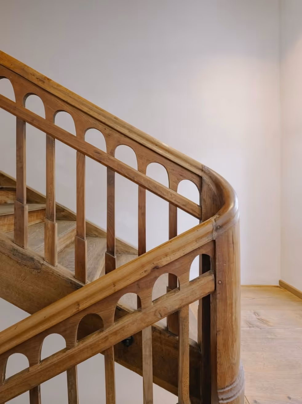 Modern bathroom featuring a wooden soaking tub, a potted green plant, wooden stool, and slatted wood flooring under natural light.