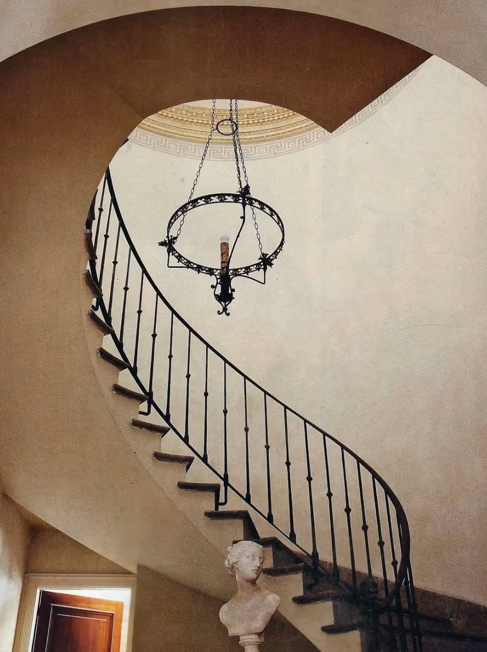 Modern bathroom featuring a wooden soaking tub, a potted green plant, wooden stool, and slatted wood flooring under natural light.