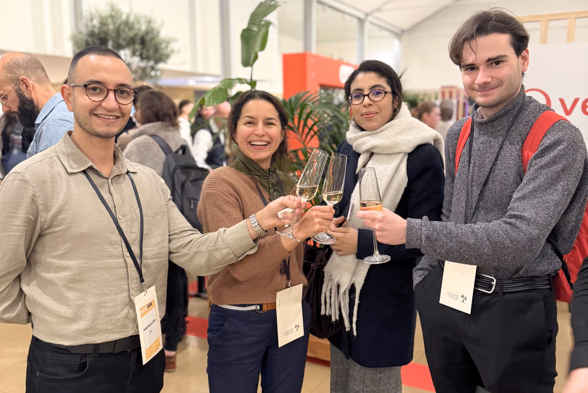 Quatre jeunes adultes souriants portent un toast avec des flûtes de champagne lors d'un événement en intérieur.