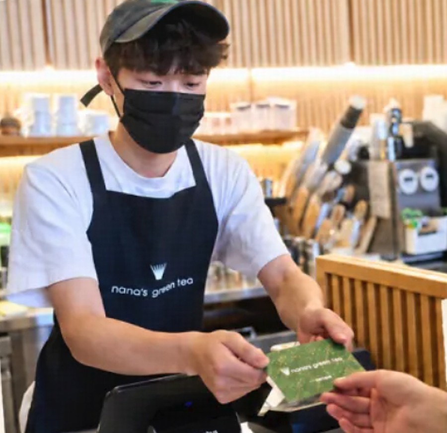 Nana's Green Tea的店员隔着柜台把一张绿色礼品卡递给客人