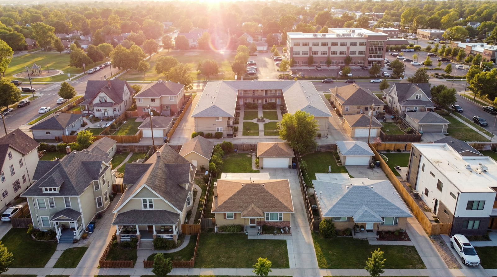 Aerial drone view of mixed residential and commercial neighborhood at golden hour showing diverse property types