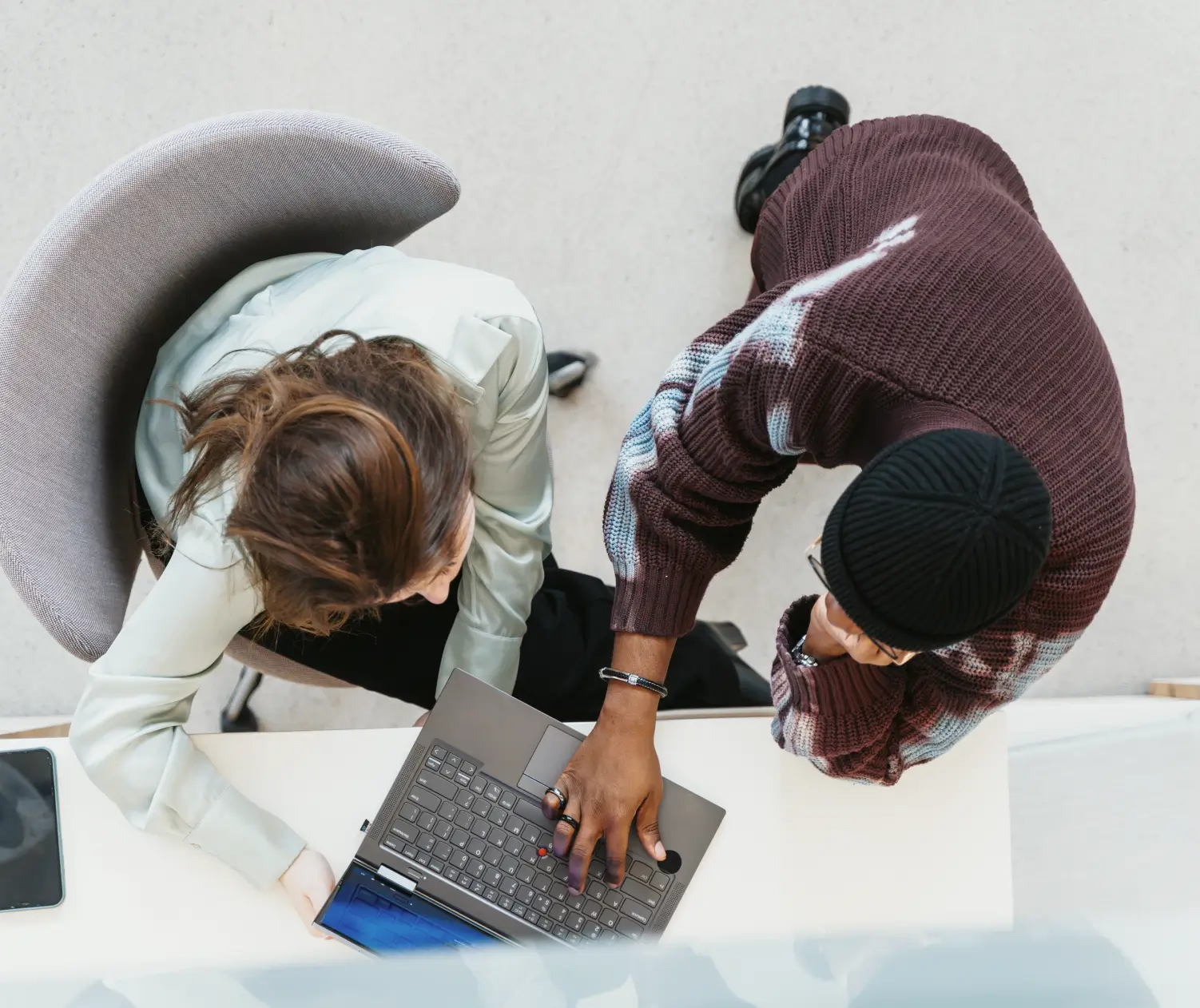 Duas pessoas vistas de cima olhando para uma tela de laptop em uma mesa branca.