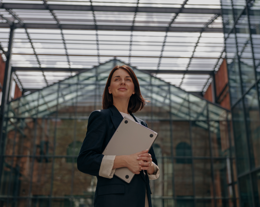 Mulher confiante segurando um laptop em um edifício moderno com estrutura de vidro.