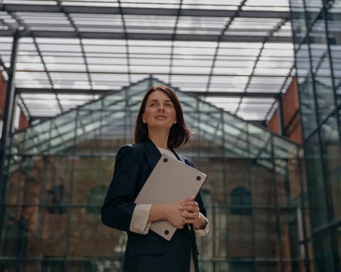 Mulher confiante segurando um laptop em um edifício moderno com estrutura de vidro.