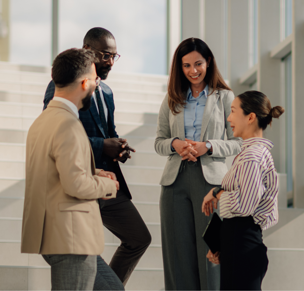 Quatro colegas de trabalho conversando alegremente em um ambiente de escritório iluminado.