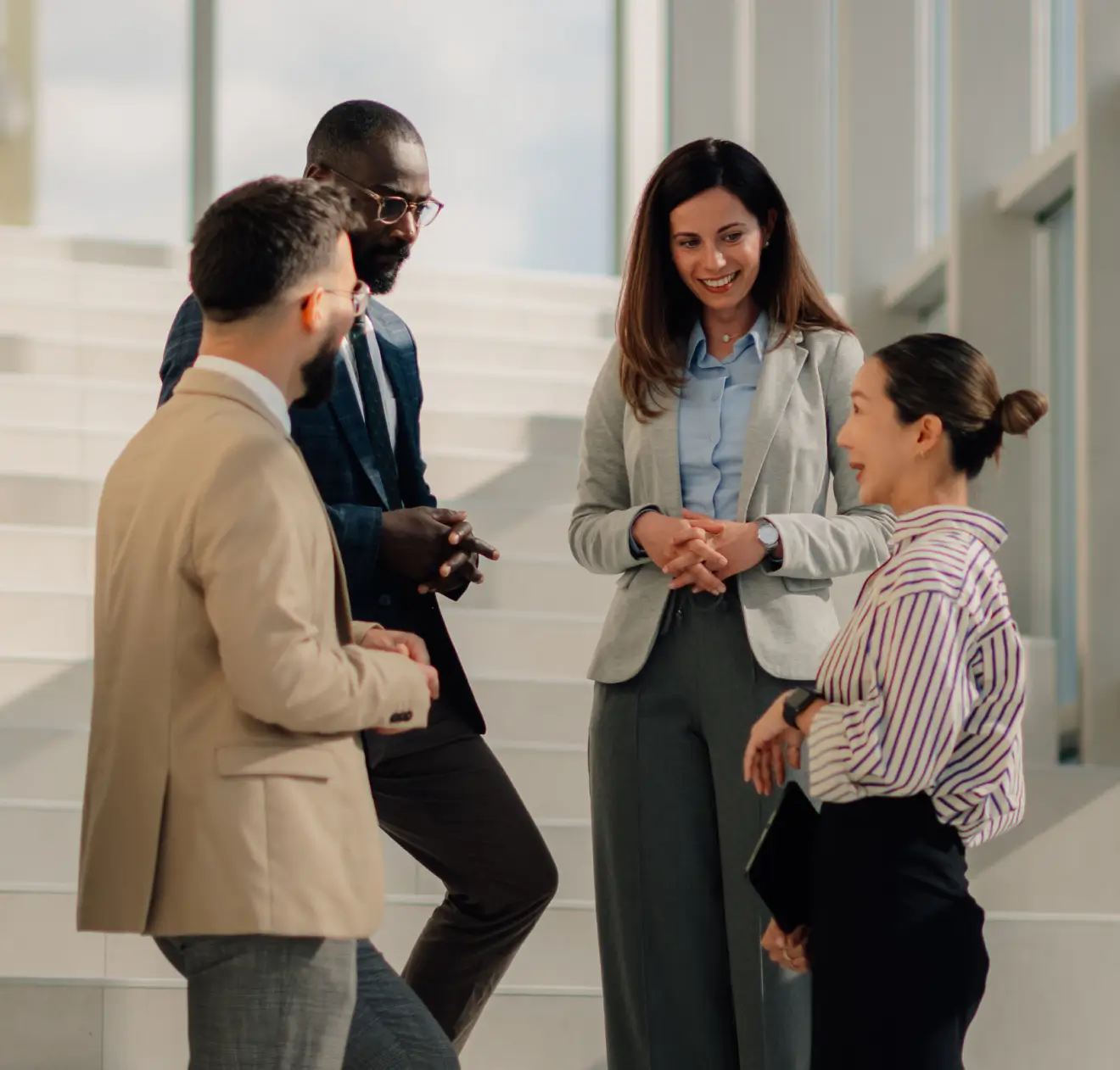 Quatro colegas de trabalho conversando alegremente em um ambiente de escritório iluminado.