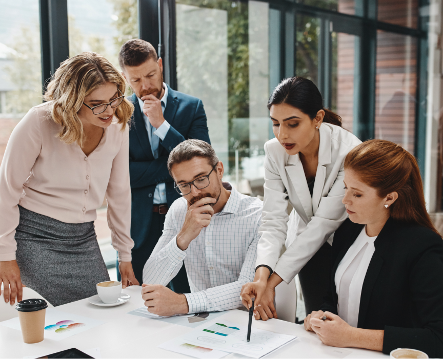 Quatro profissionais discutindo gráficos e documentos em uma mesa de reunião em escritório moderno.
