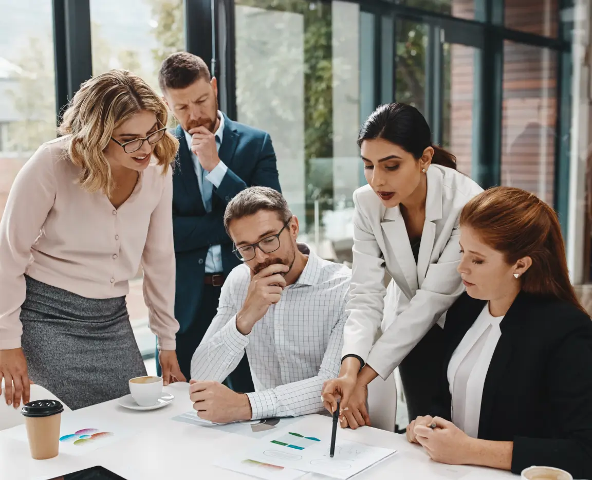 Quatro profissionais discutindo gráficos e documentos em uma mesa de reunião em escritório moderno.