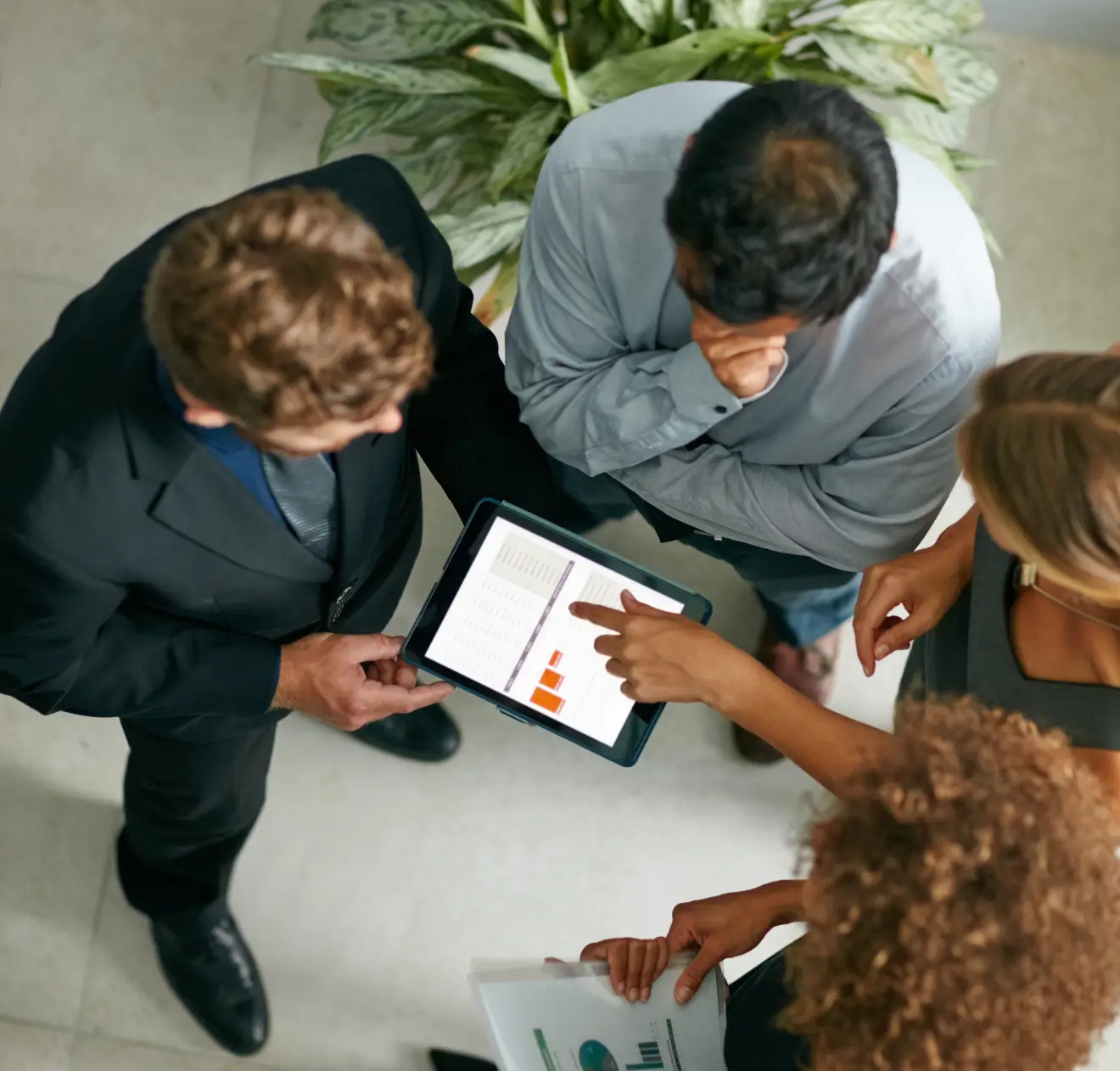 Quatro pessoas em pé olhando para um tablet com gráficos e tabelas, discutindo informações.