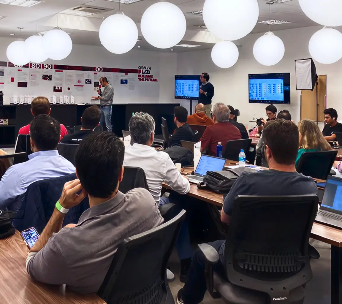 Pessoas em uma sala de reuniões assistindo a apresentação de dois homens com telas exibindo gráficos.