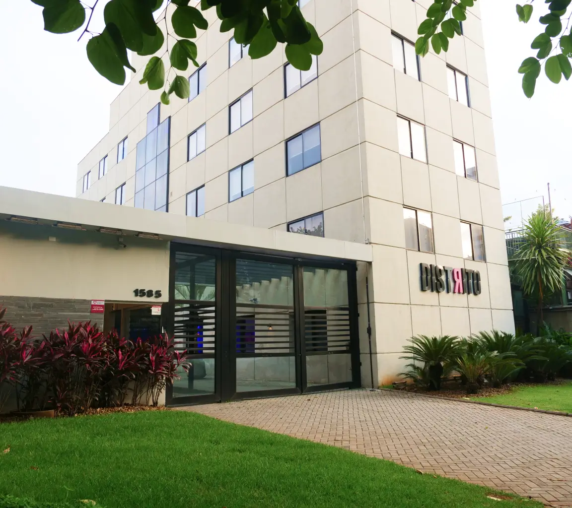 Fachada de edifício comercial moderno com entrada de vidro, árvores ao redor e o número 1585 visível na parede.