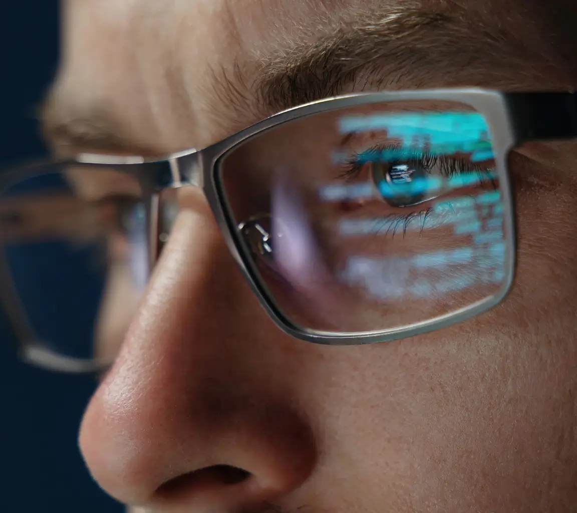 Close-up de rosto de pessoa usando óculos refletindo linhas de código em azul.