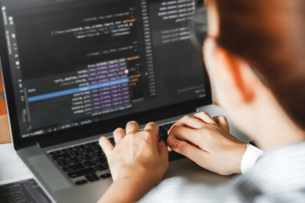 Pessoa digitando código em um laptop com editor de programação aberto na tela.