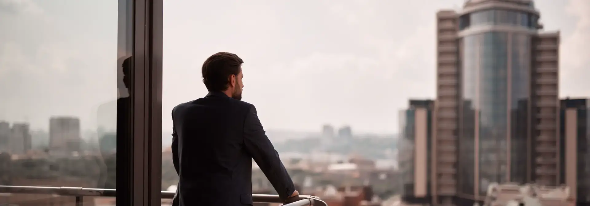 Homem de terno olhando para a vista da cidade a partir de uma sacada com corrimão de metal.