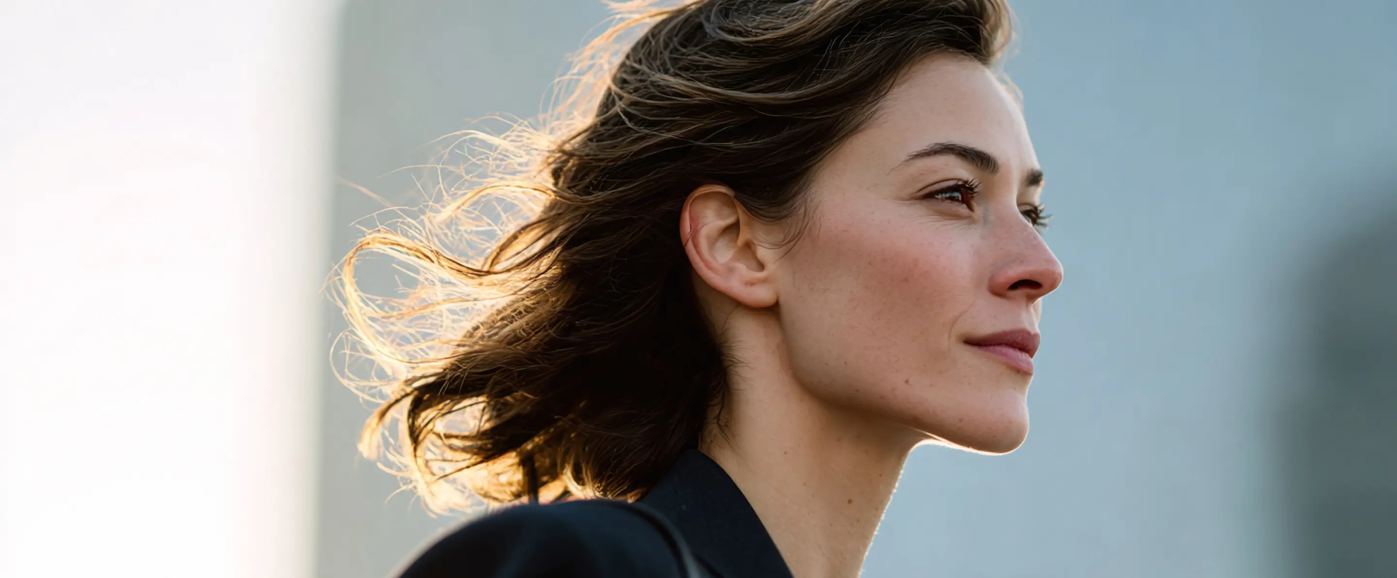 Mulher olhando para a distância com vento soprando seus cabelos castanhos ao fundo desfocado.