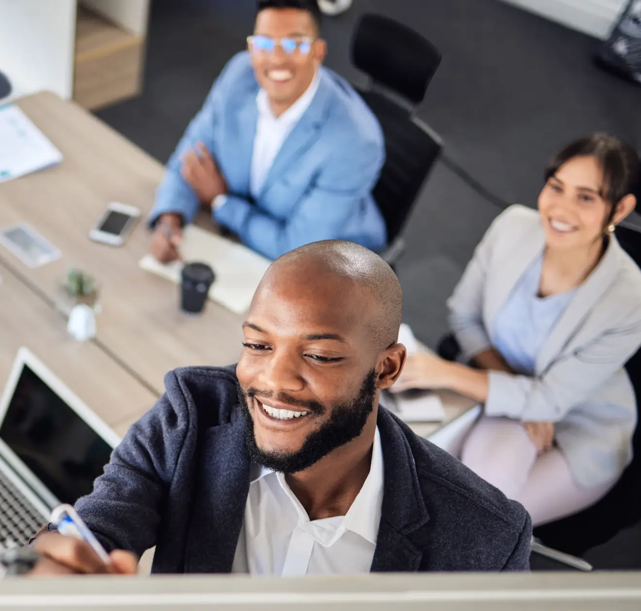 Três profissionais sorridentes discutindo ideias em frente a um quadro branco no escritório.