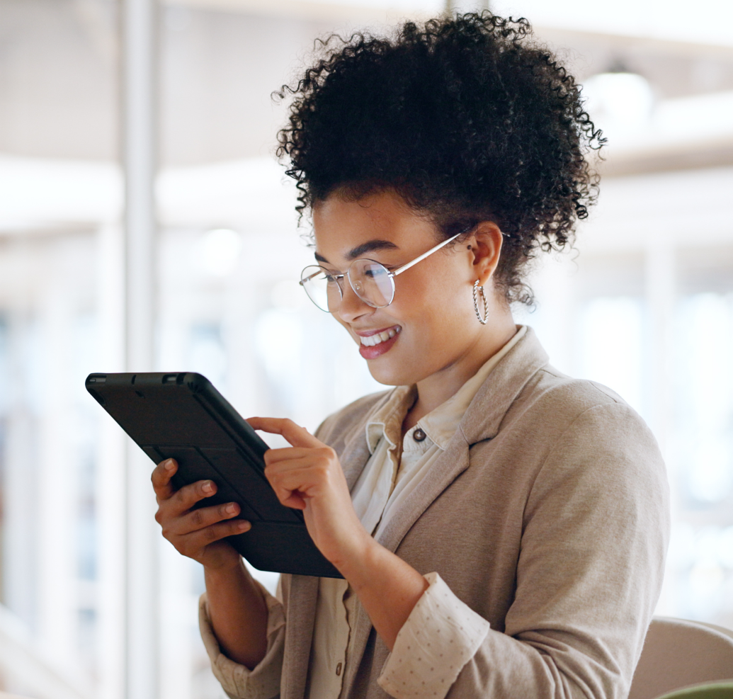 Mulher sorridente com óculos usando tablet em ambiente de escritório moderno.