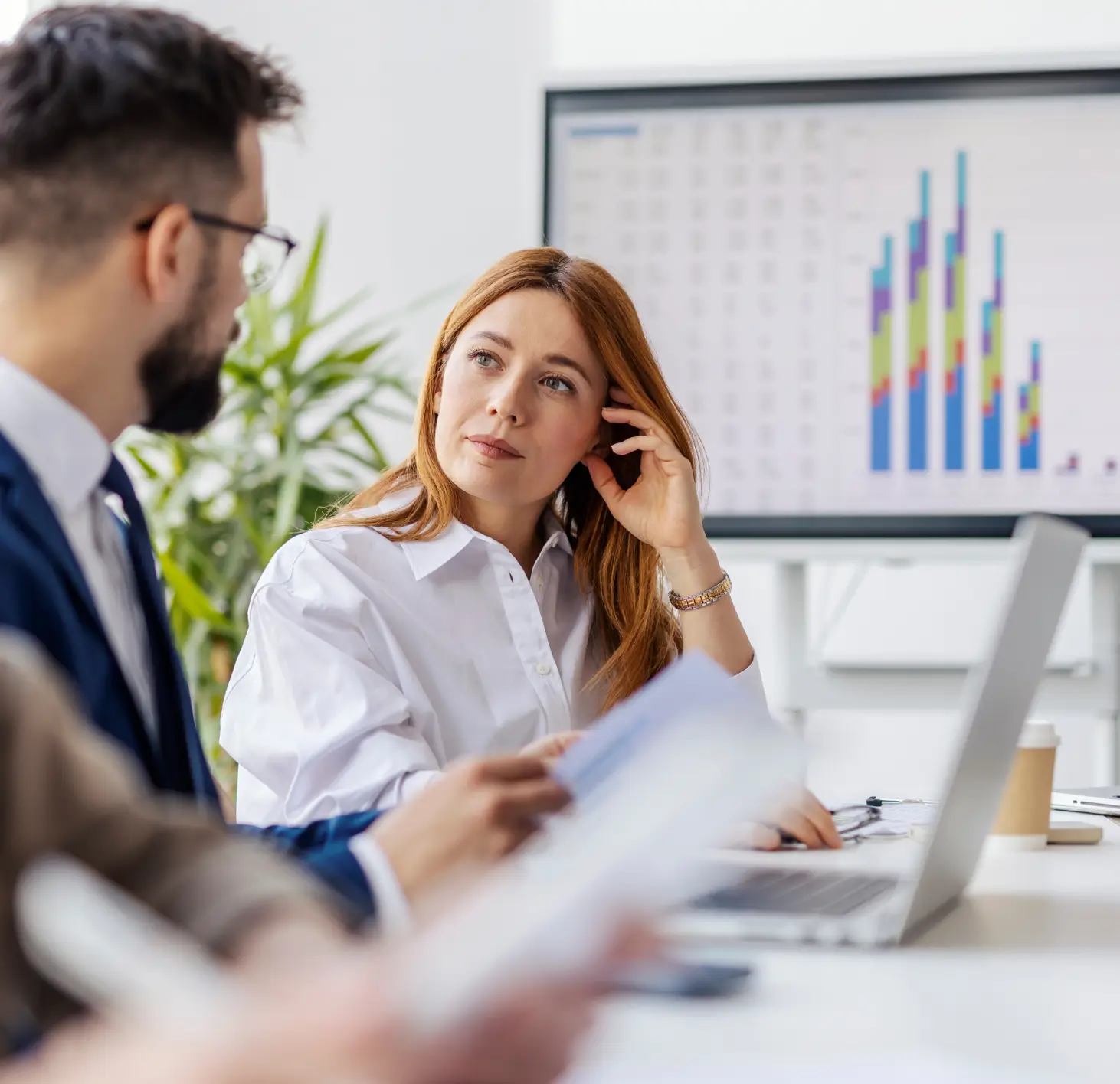 Mulher observando atenta um homem durante reunião de trabalho com gráfico colorido na tela ao fundo.