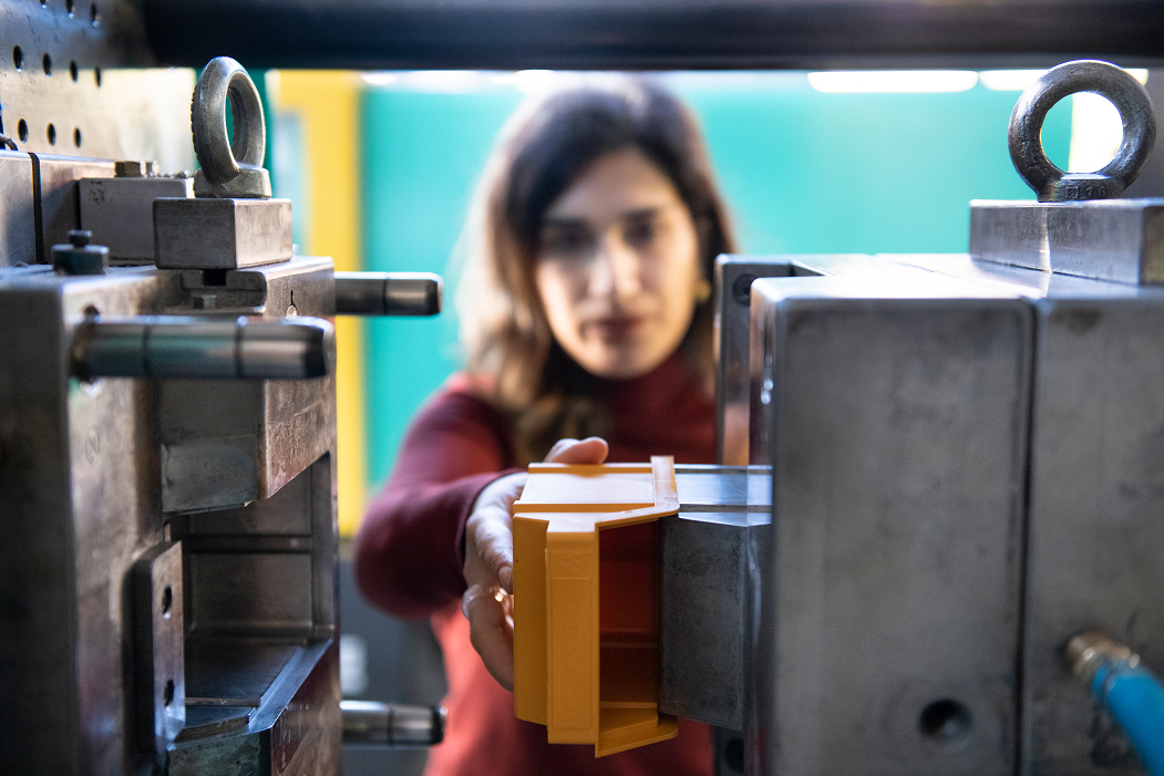 Mitarbeiterin entnimmt ein Kunststoffbauteil aus einer Spritzgießmaschine