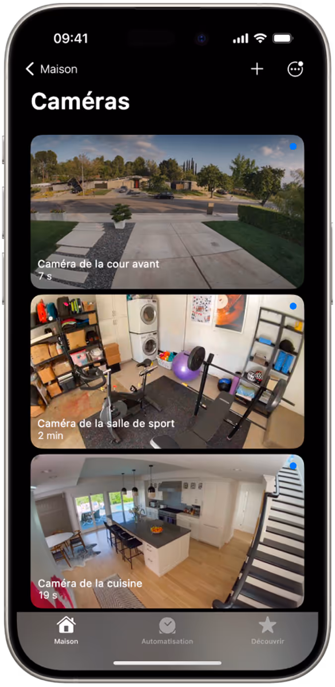 Écran de smartphone affichant les images des caméras : jardin, salle de sport et cuisine, avec horodatage. L'interface inclut des options de navigation.