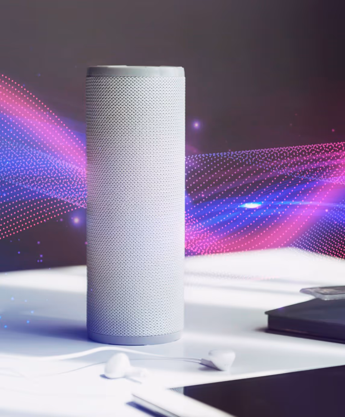 Une enceinte connectée cylindrique blanche posée sur un bureau, avec des ondes sonores colorées en arrière-plan. Des écouteurs et une tablette sont à proximité.