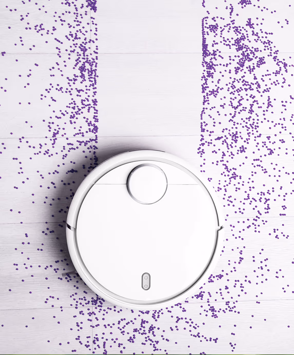 Un aspirateur domotique robot blanc sur un sol en bois clair, entouré de confettis violets dispersés.