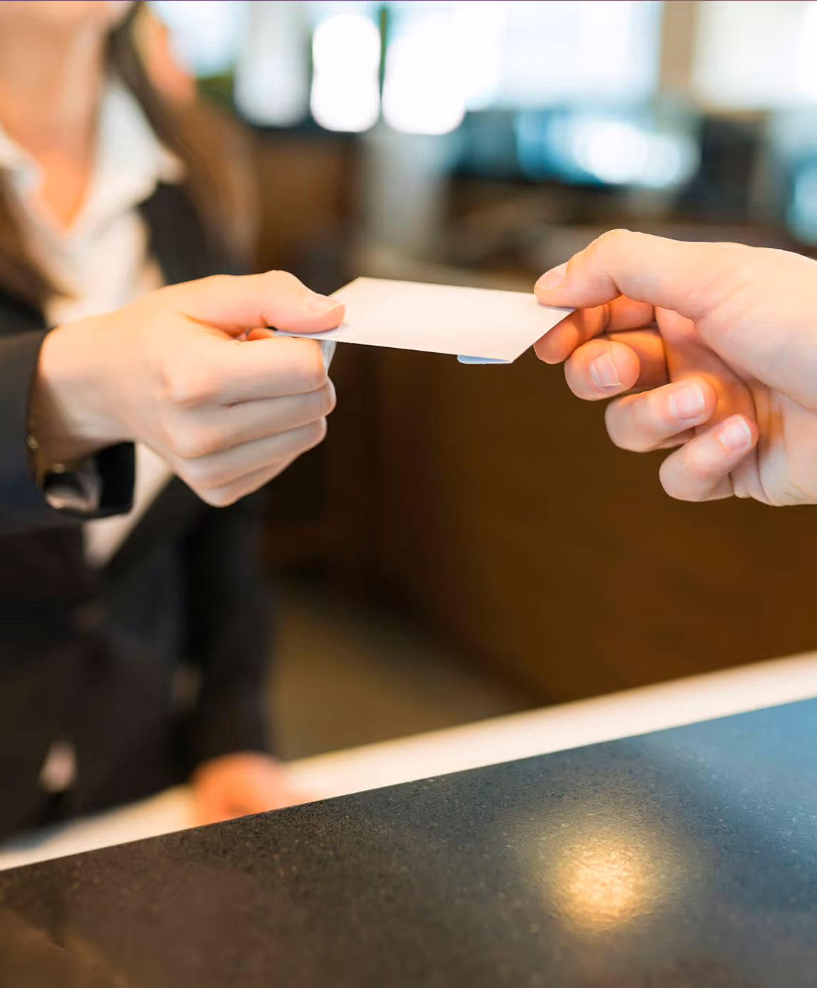 Une réceptionniste d'hôtel remet une carte vierge à un client sur un comptoir sombre.