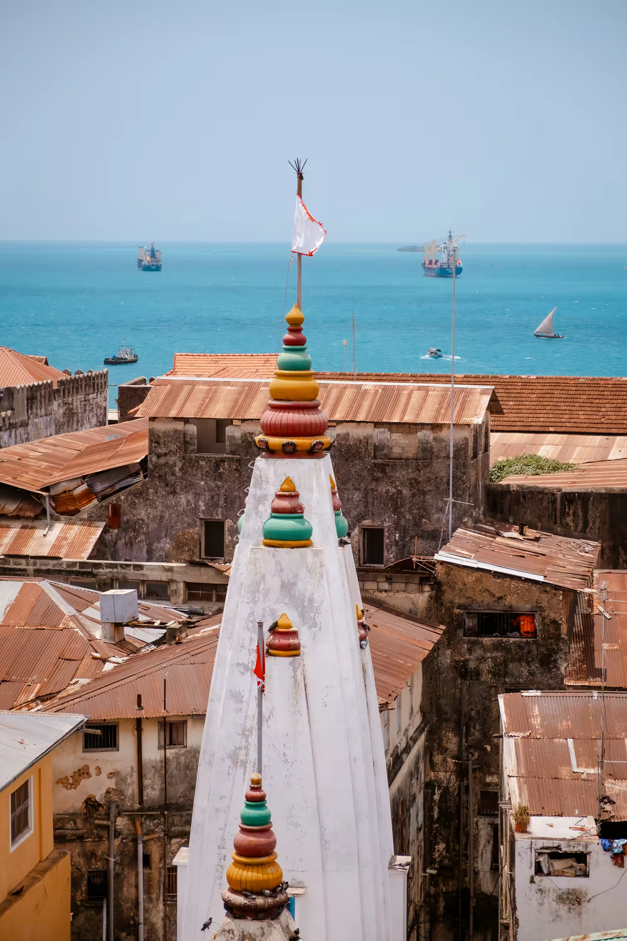 Stone Town skyline with colorful mosque towers, old buildings, and ships on turquoise ocean water.
