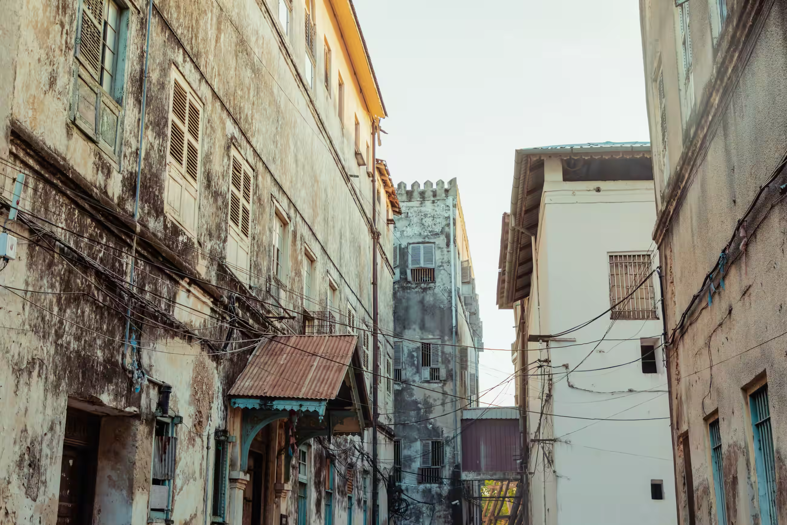 A lively street scene in Zanzibar featuring members of traditional Zanzibar tribes in a vibrant outdoor market. The individuals are dressed in colorful traditional clothing, reflecting their cultural heritage, and are engaged in activities such as selling goods and interacting with one another. The background includes a mix of market stalls with baskets, textiles, and other items for sale, set against a backdrop of buildings with a warm, earthy tone. The atmosphere is bustling yet warm, capturing the essence of a community gathering of traditional Zanzibar tribes