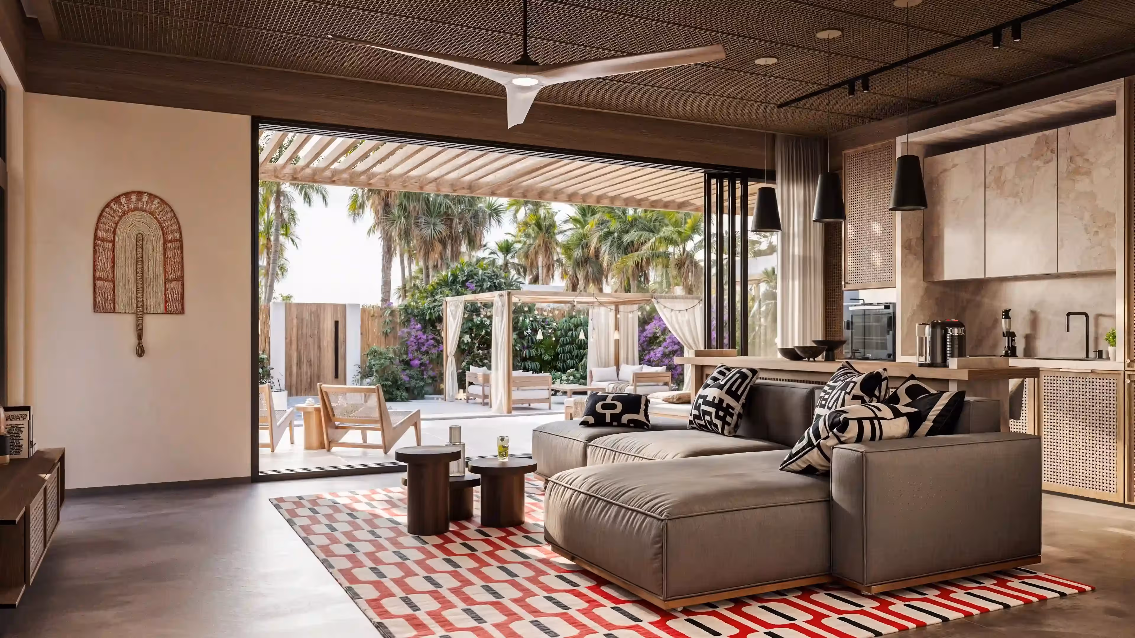Modern living room with gray sectional sofa, patterned rug, and sliding open doors showing outdoor seating and palm trees.