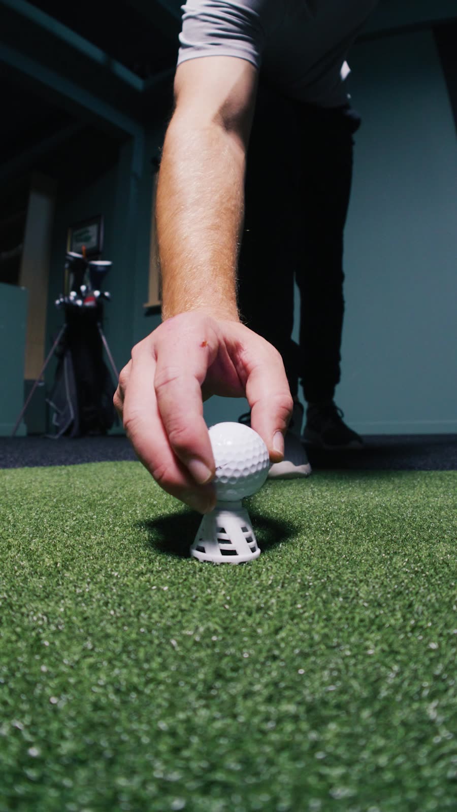 A hand teeing up a ball on the hitting mat