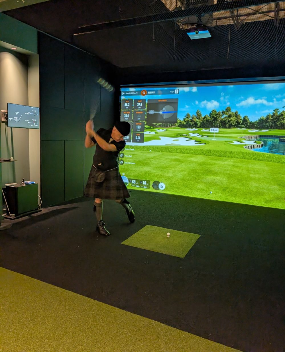 A golfer in a kilt and tam o' shanter driving off the tee in a SWINGS bay
