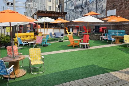 Outdoor patio with vintage lawn chairs, orange umbrellas and a mural-backed brick wall at Lonesome Dove Knoxville