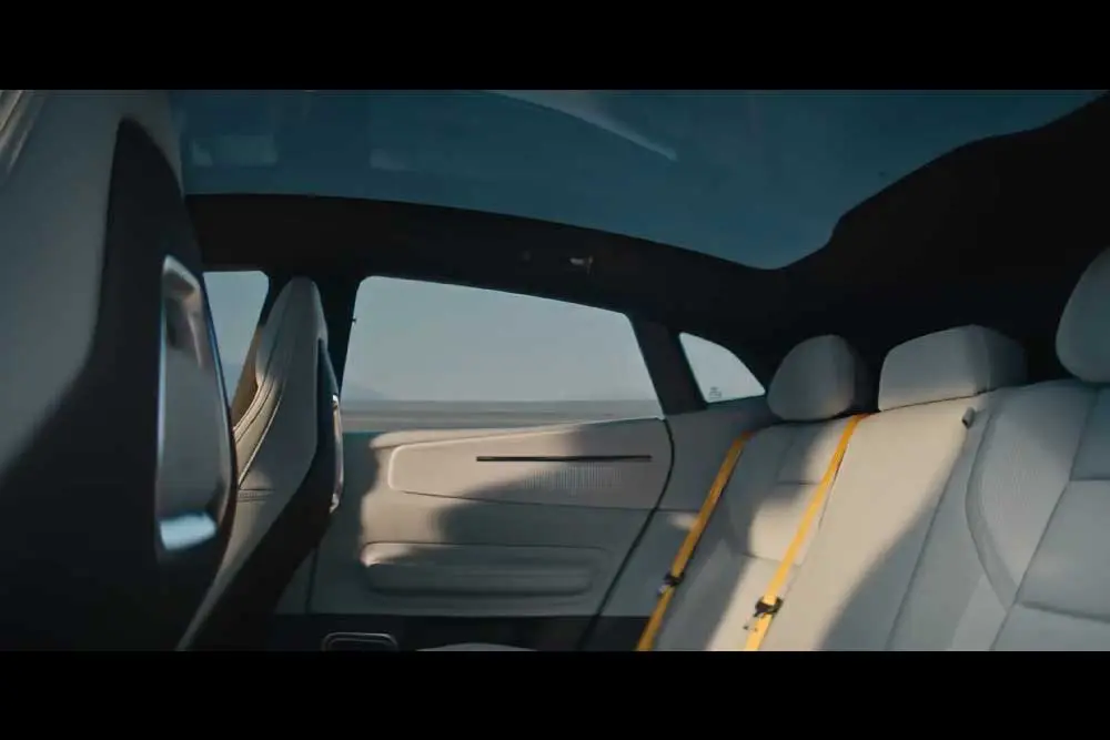 Der Innenraum eines modernen Autos, gesehen von der Rückbank. Die Sitze sind weiss, das Dach besteht aus Glas und man kann die offene Landschaft durch die Fenster sehen.