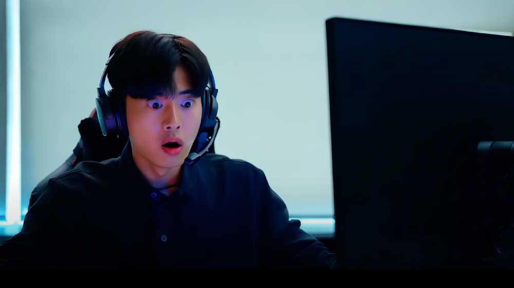 Ein junger Mann mit Headset starrt mit weit aufgerissenen Augen auf einen Computermonitor. Er sitzt vor einem dunklen Hintergrund, der von bläulichem Licht beleuchtet wird.