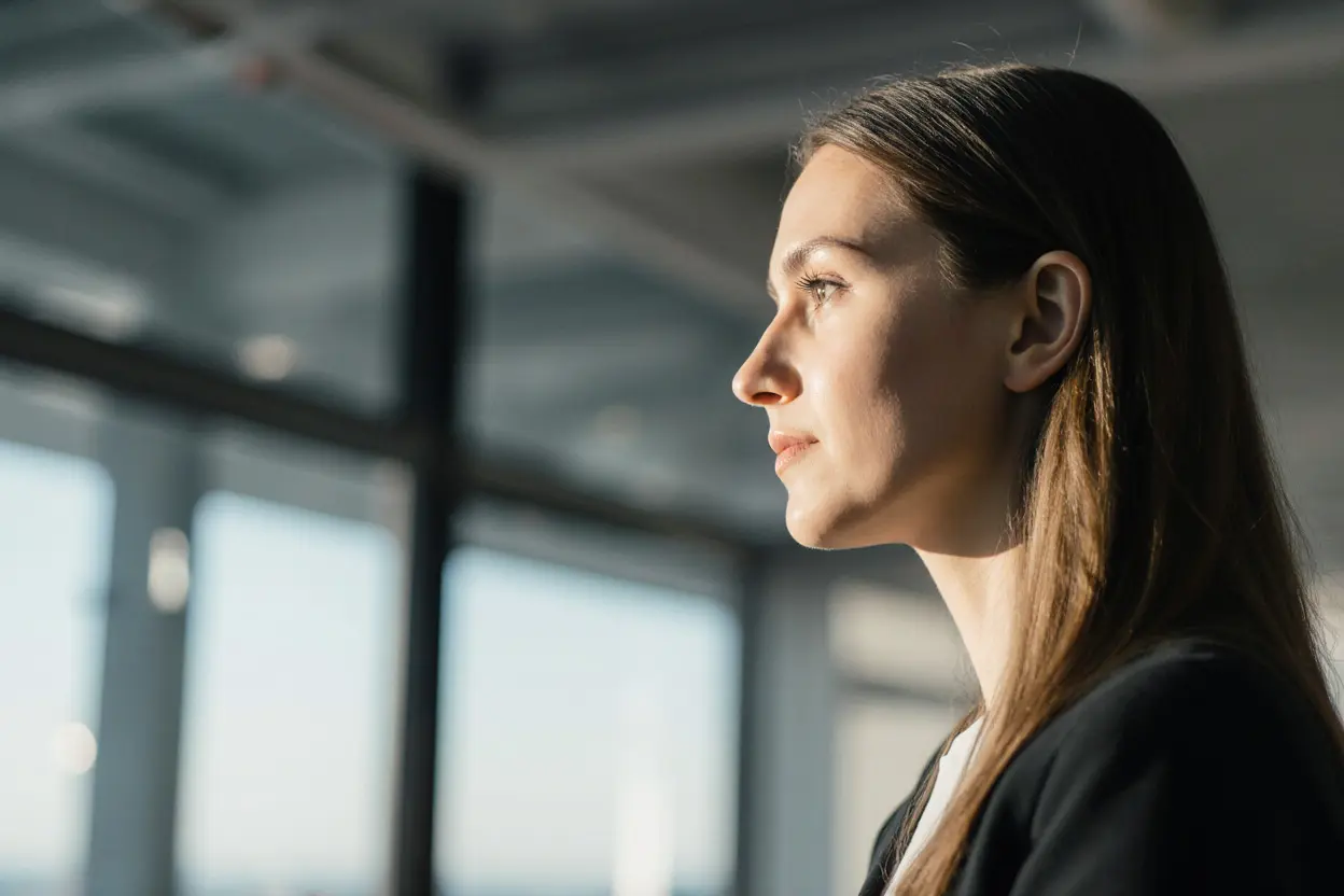 Profilansicht einer Frau im Business-Look, blickend in die Sonne am Fenster.