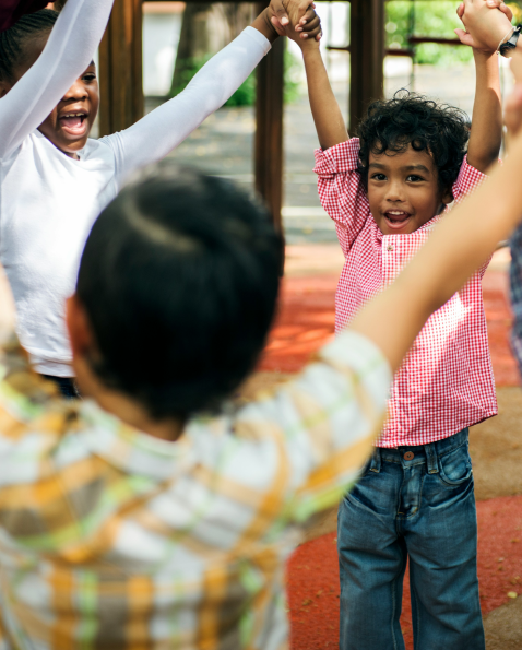 Children holding hands and playing outdoors, smiling and having fun.