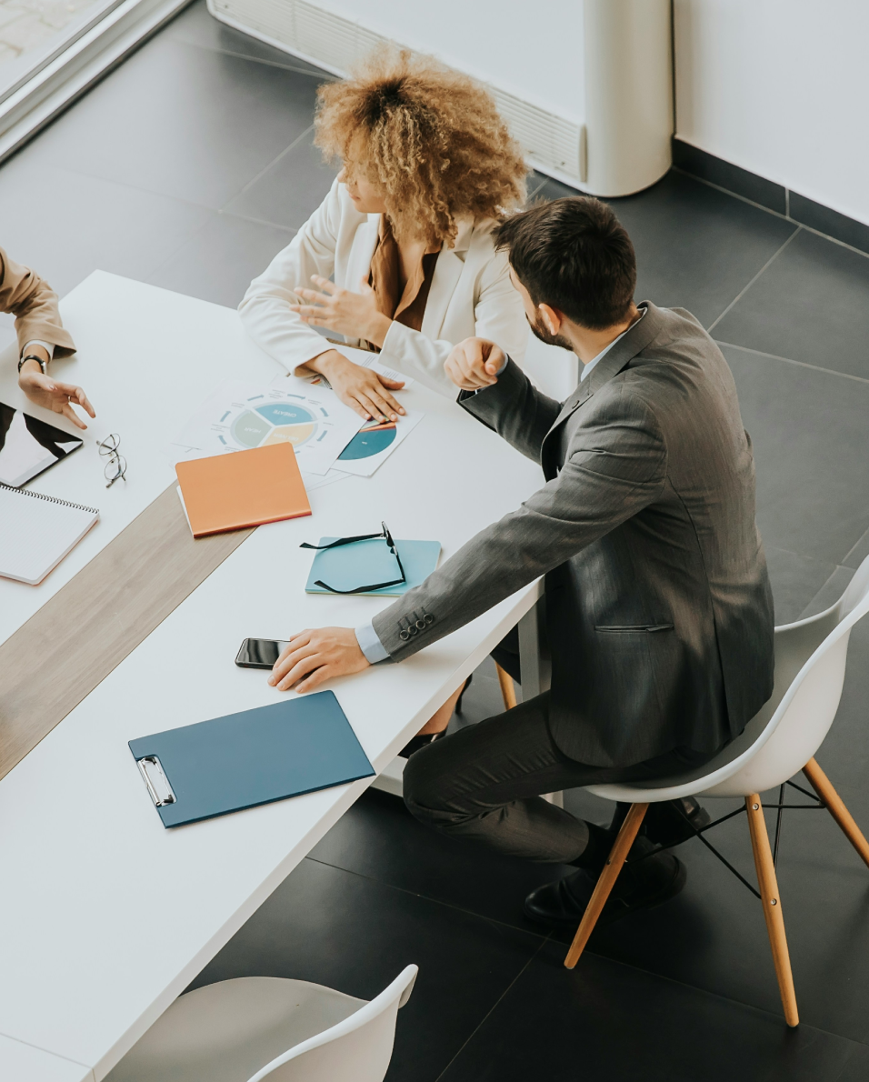 Two business professionals sitting at a white table discussing charts and documents during a meeting.