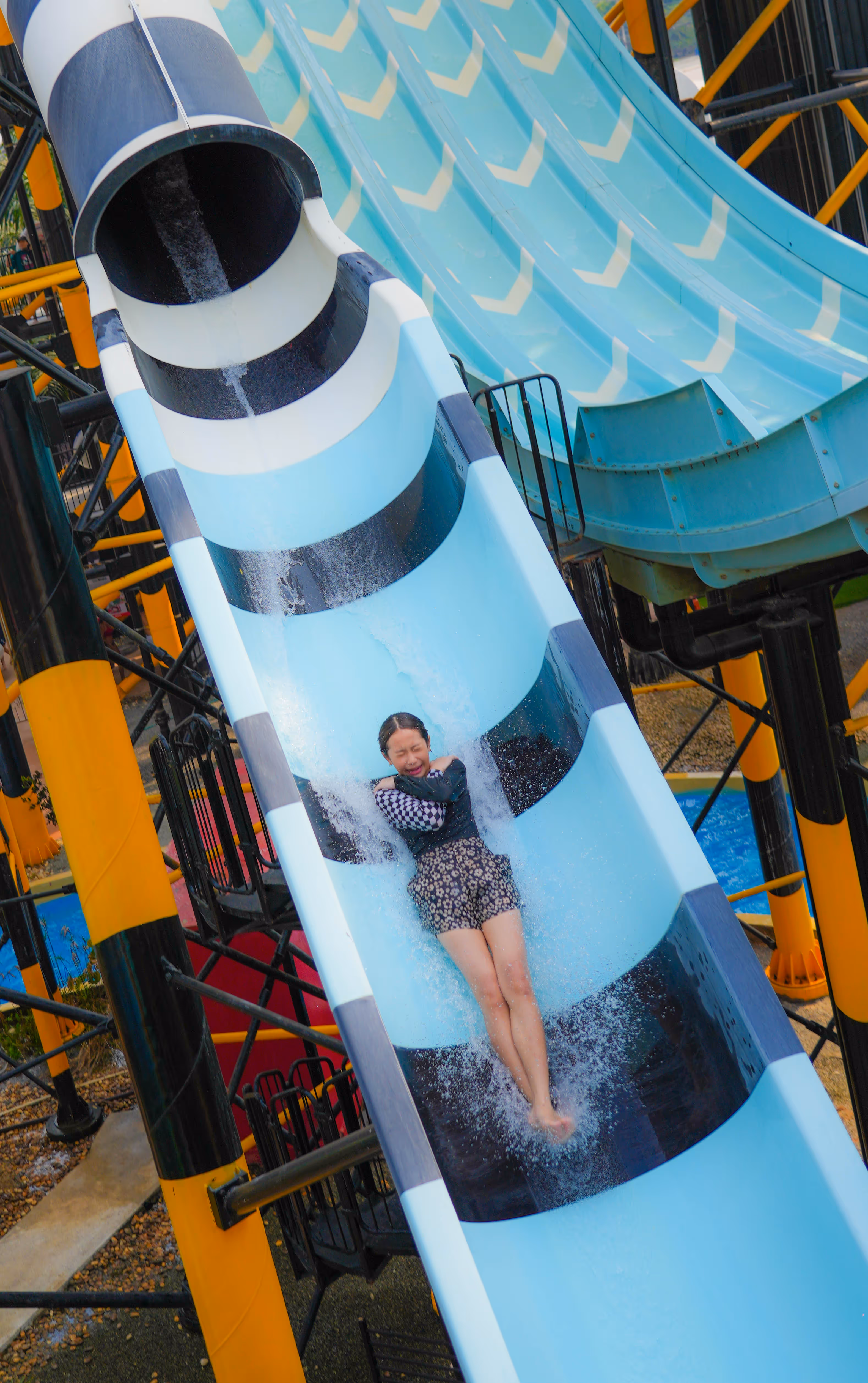 Smiling couple posing in front of a bright green Ghostbusters-themed water slide at Aquaverse, with a large Slimer figure overhead and a themed inner tube in hand.