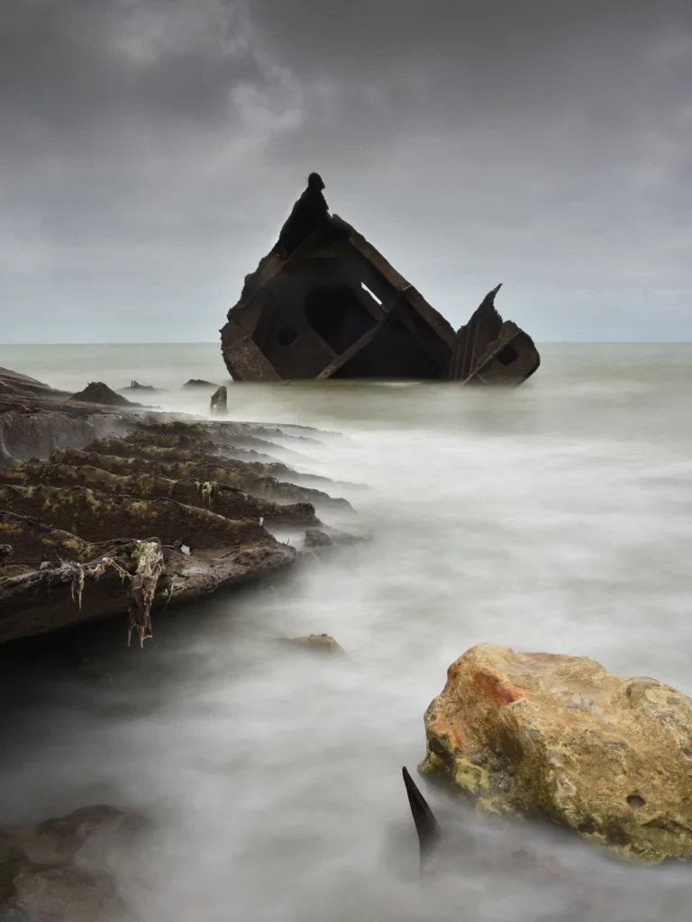 Echoué sur une plage, durant le débarquement en Normandie, les restes d'un bateau sur l'eau, classé 13ème au concours photo WinSPOT by Data Concept 2023-2024