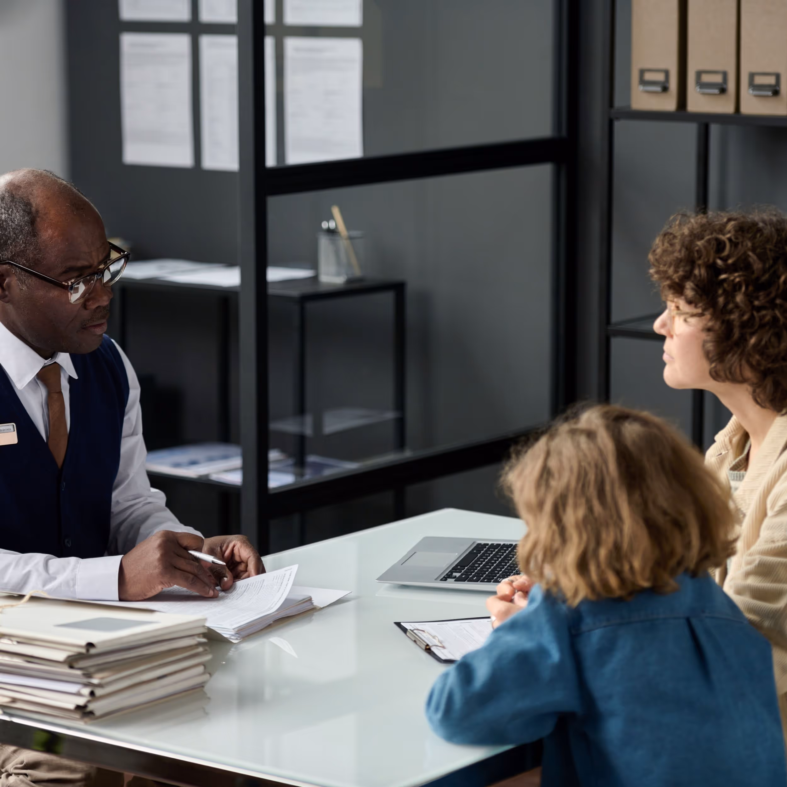 Benefits advisor talks to mother and daughter across a desk stacked with papers.