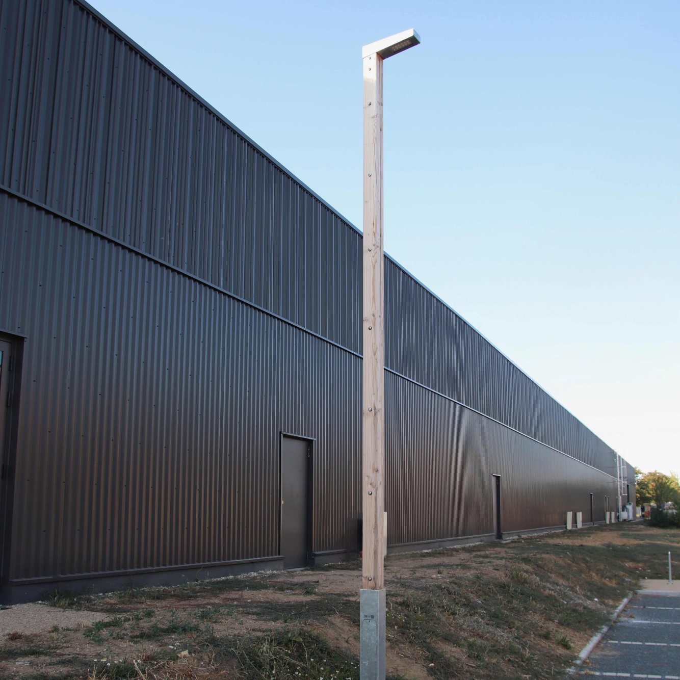 Mât d'éclairage Buho en bois douglas le long d'un bâtiment commercial à Saint-Cyr-sur-Loire