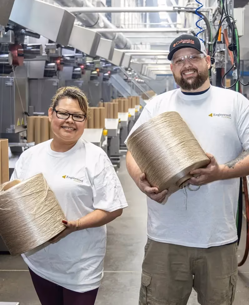 Two plant workers holding large spools of yarn on the production floor
