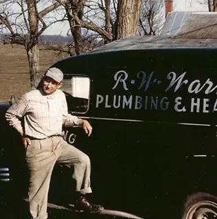 Vintage plumber leaning against work van with business signage